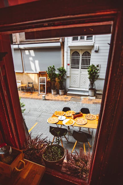 View of an inviting outdoor pizzeria with tables set for dining on a quiet street. Perfect spot for a meal.